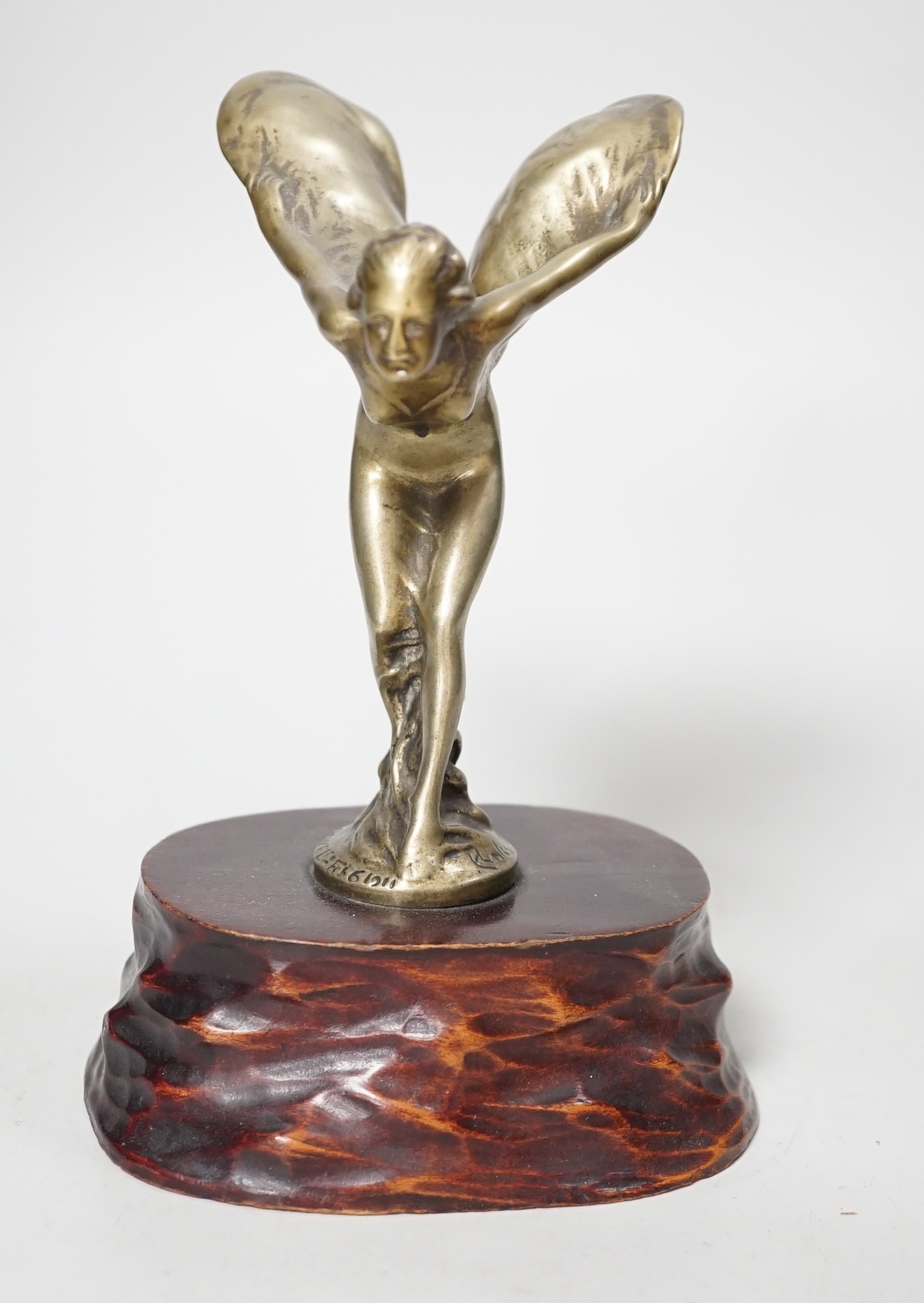 After Charles Sykes, a gilt metal Rolls Royce car mascot - ‘’Spirit of Ecstasy’’, inscribed and bearing date 1911, on a carved wooden plinth. 17.5cm tall